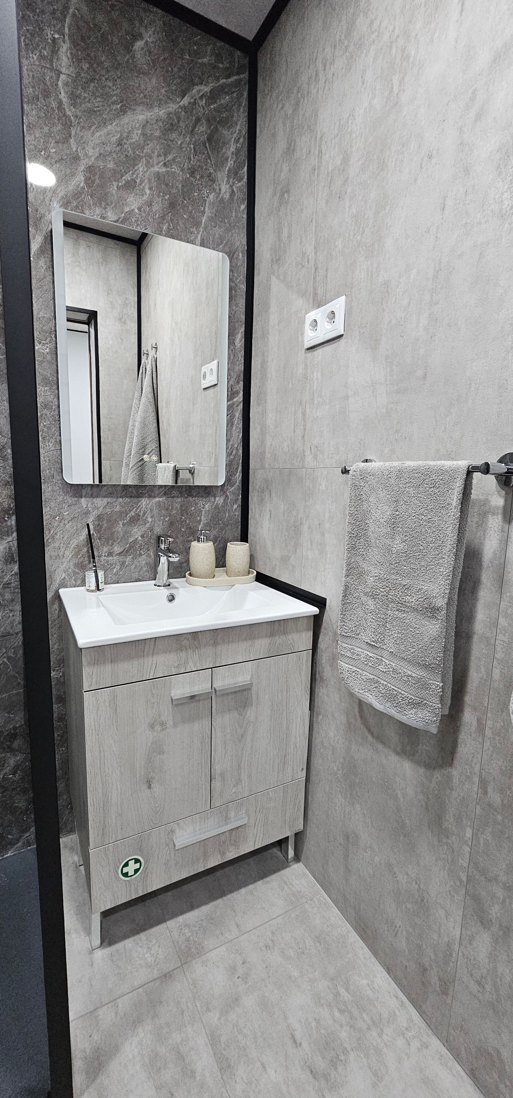 A modern bathroom with a marble wall, a wooden vanity, a mirror, and a towel rack.