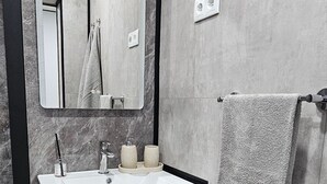 A modern bathroom with a marble wall, a wooden vanity, a mirror, and a towel rack. - Charming 1-bedroom Apartment With Ocean Views in Calheta (Calheta)