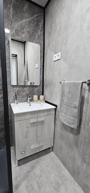 A modern bathroom with a marble wall, a wooden vanity, a mirror, and a towel rack. - Charming 1-bedroom Apartment With Ocean Views in Calheta (Calheta)