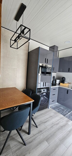 Eine moderne Küche mit integrierten Geräten, ein Essbereich mit Holztisch und Stühlen sowie eine hängende Leuchte.