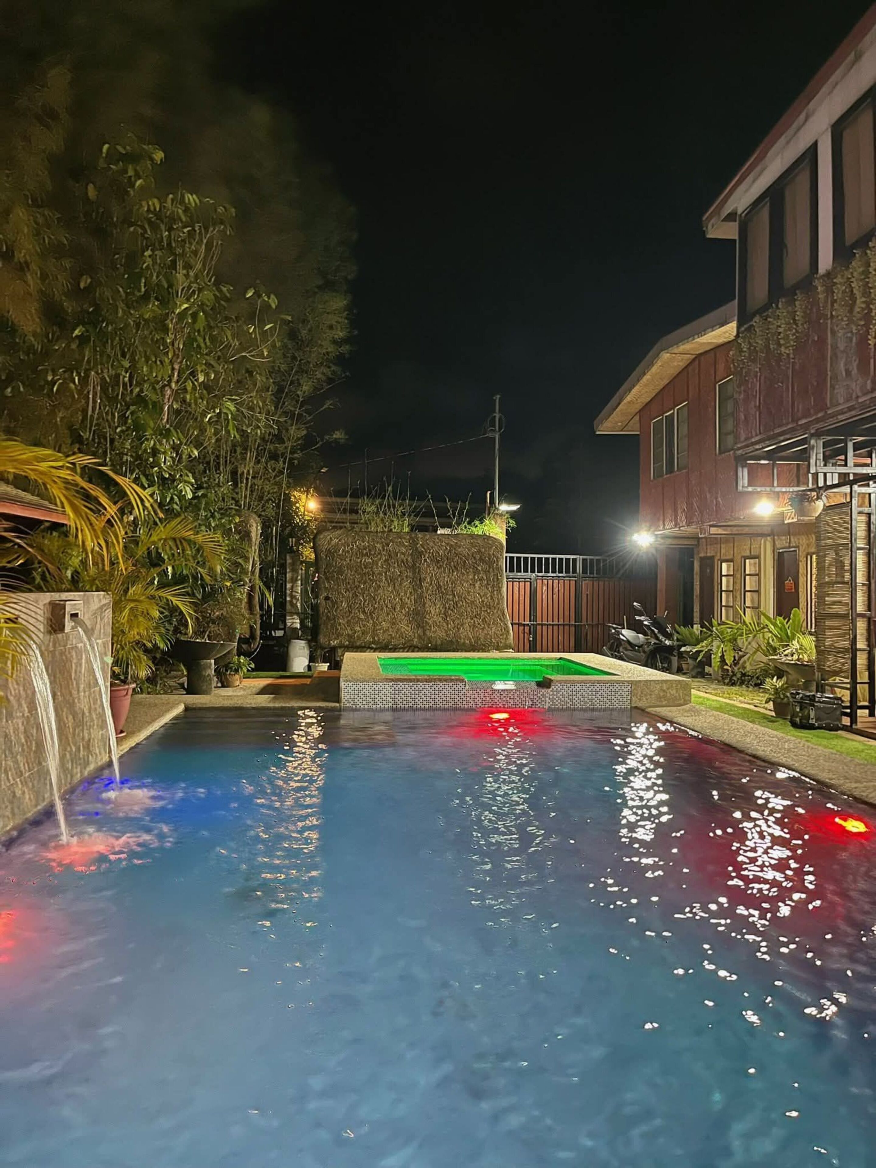 Una piscina con una cascada, rodeada de follaje y un edificio con balcón.