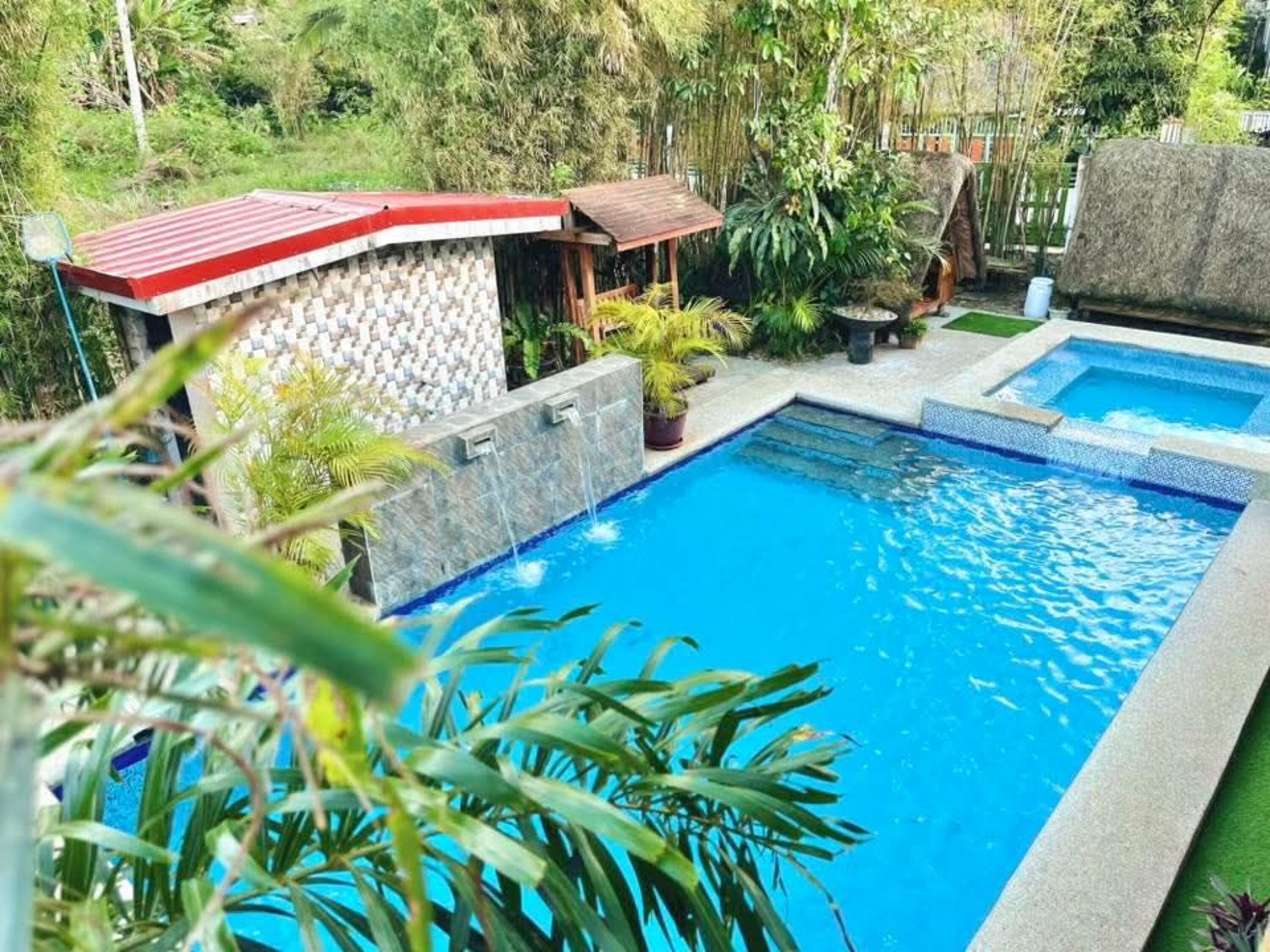 A swimming pool with a tiled edge, surrounded by greenery and a small structure with a red roof.
