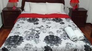 Cama com colcha floral, duas luminárias vermelhas e cabeceira de madeira.