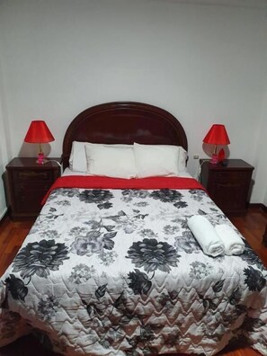 A bed with a floral quilt, two red lamps, and a wooden headboard. - Familia y Grupos Luces Navidad Vigo (Vigo)