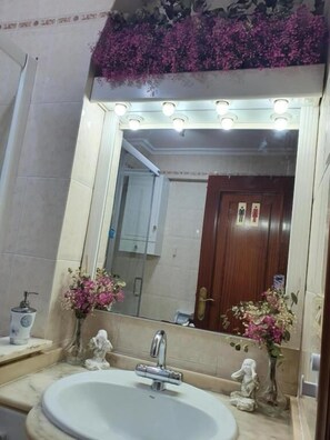 A bathroom with a large mirror, a sink, and decorative flowers. - Familia y Grupos Luces Navidad Vigo (Vigo)