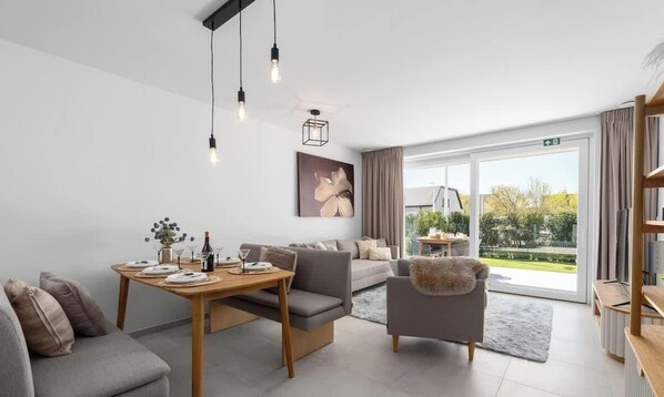 Una sala moderna con un sofá, una mesa de comedor y una silla. Hay un ventanal con vistas a la vegetación.