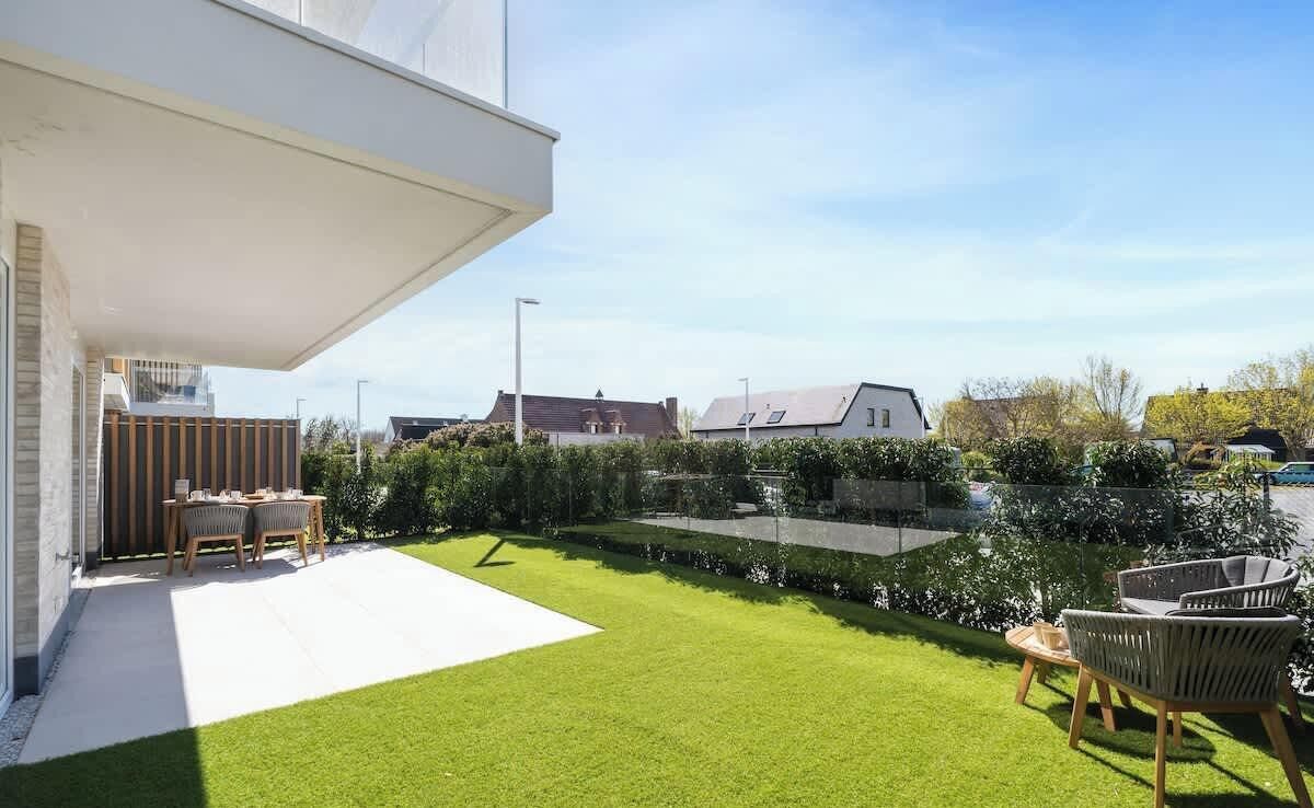 A modern house with a patio, a lawn, and a wooden fence.