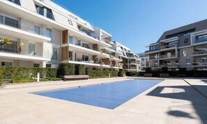 Un moderno complejo de apartamentos con varios balcones, piscina y jardín bien cuidado.