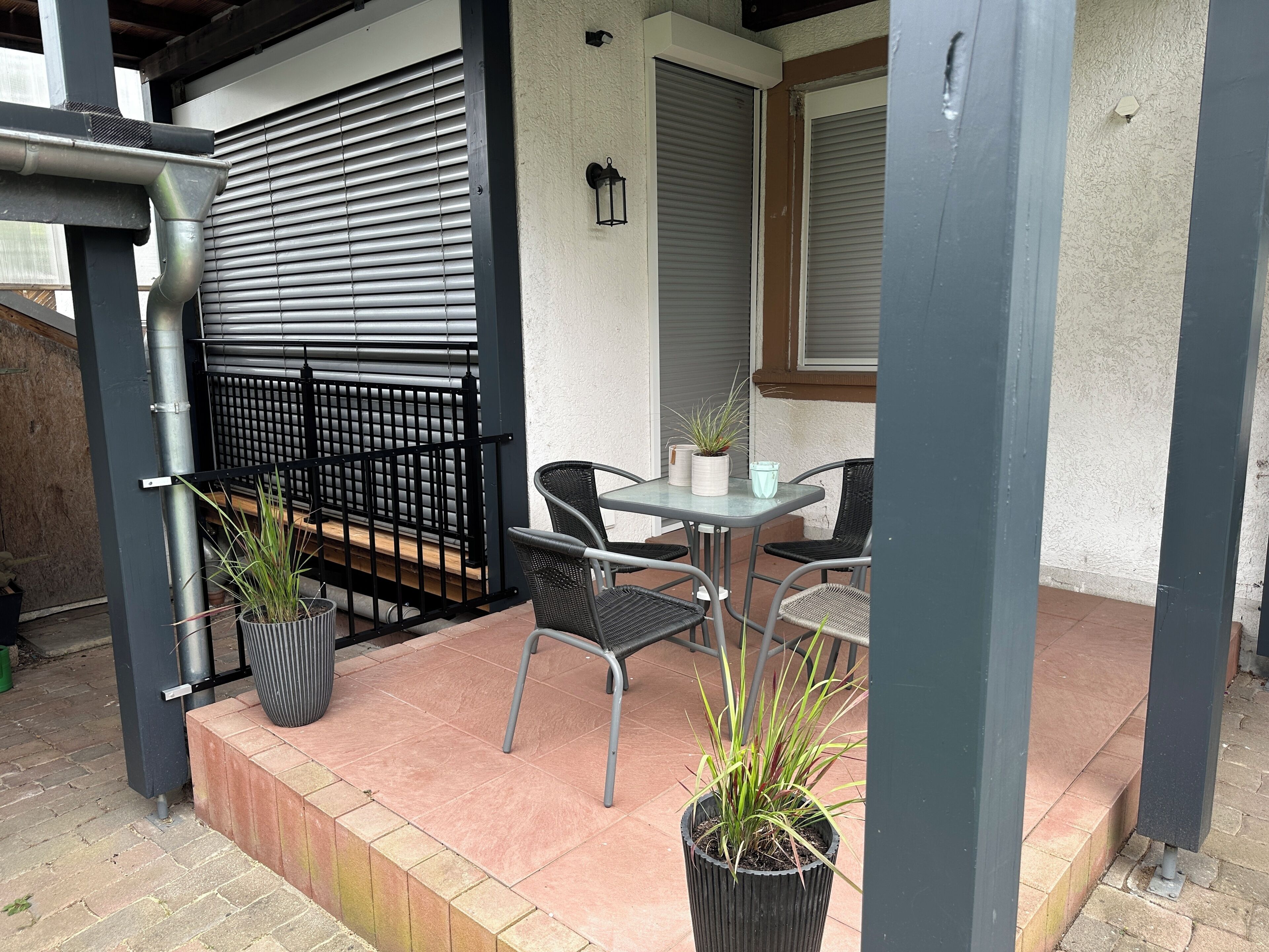 A patio area with a table and chairs, a black metal fence, and potted plants.