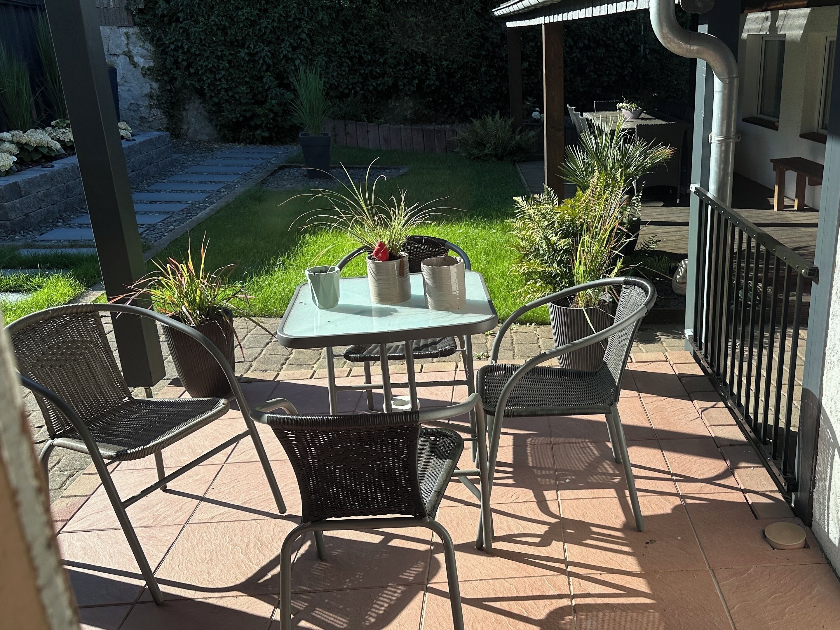 A patio with a table and chairs, surrounded by potted plants and a wooden fence.