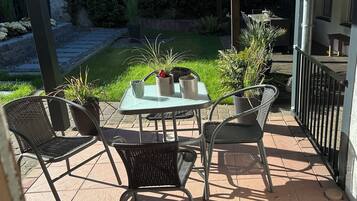 A patio with a table and chairs, surrounded by potted plants and a wooden fence.