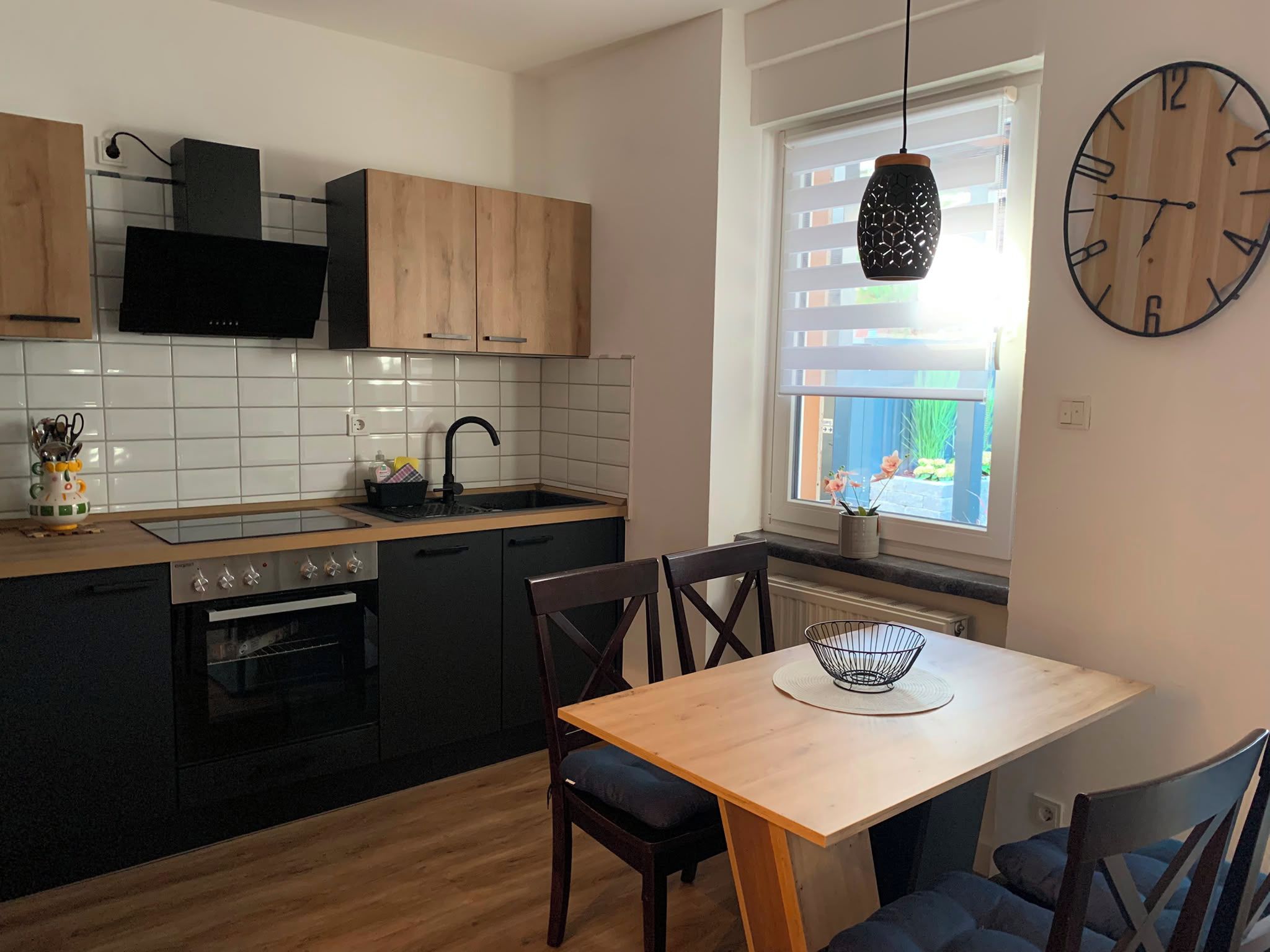 Eine moderne Küche mit Essbereich, ausgestattet mit einem schwarzen Backofen, Holzschränken und einer schwarzen Pendelleuchte.