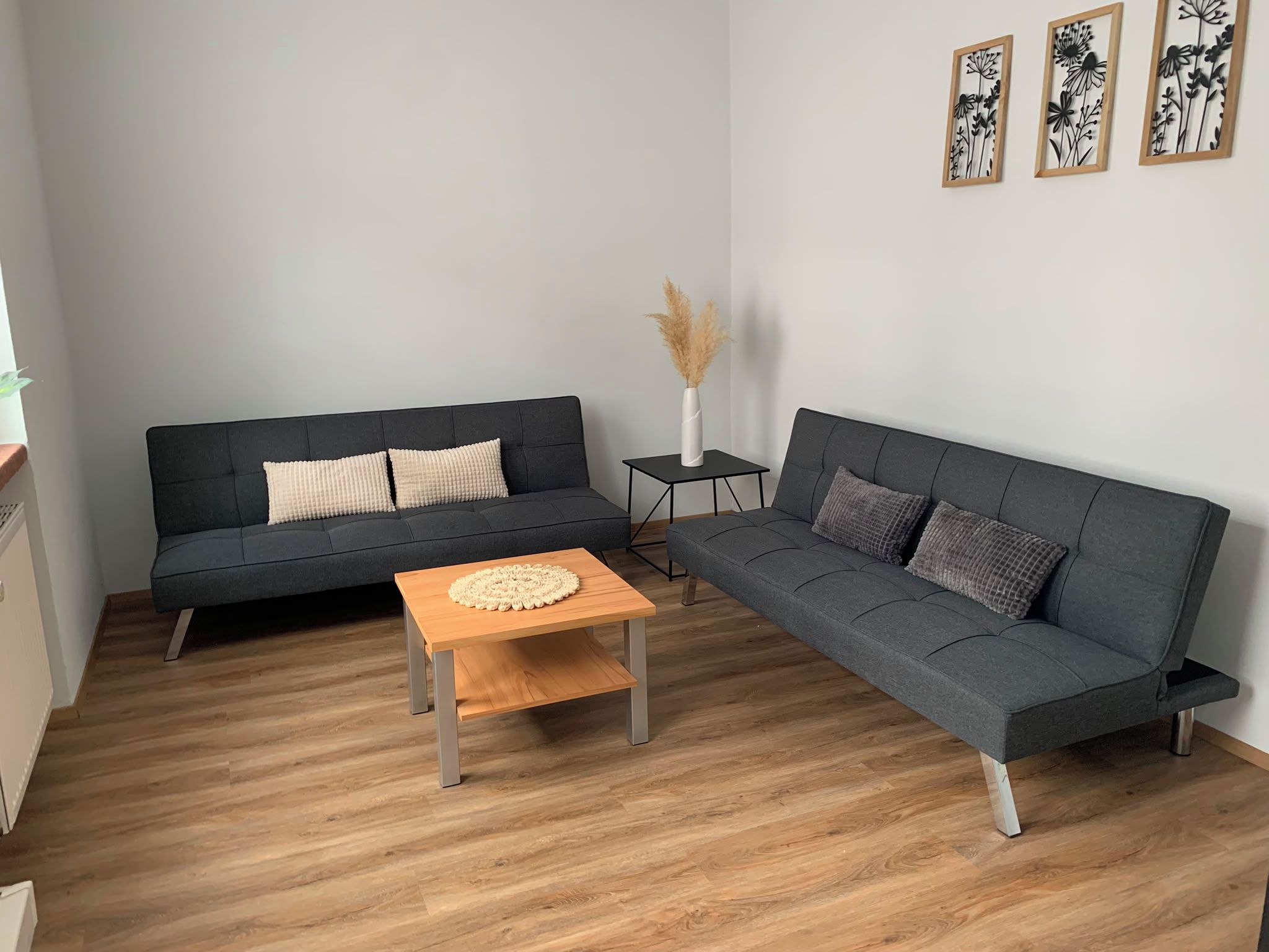 A modern living room with two grey sofas, a wooden coffee table, and a small side table with a vase.