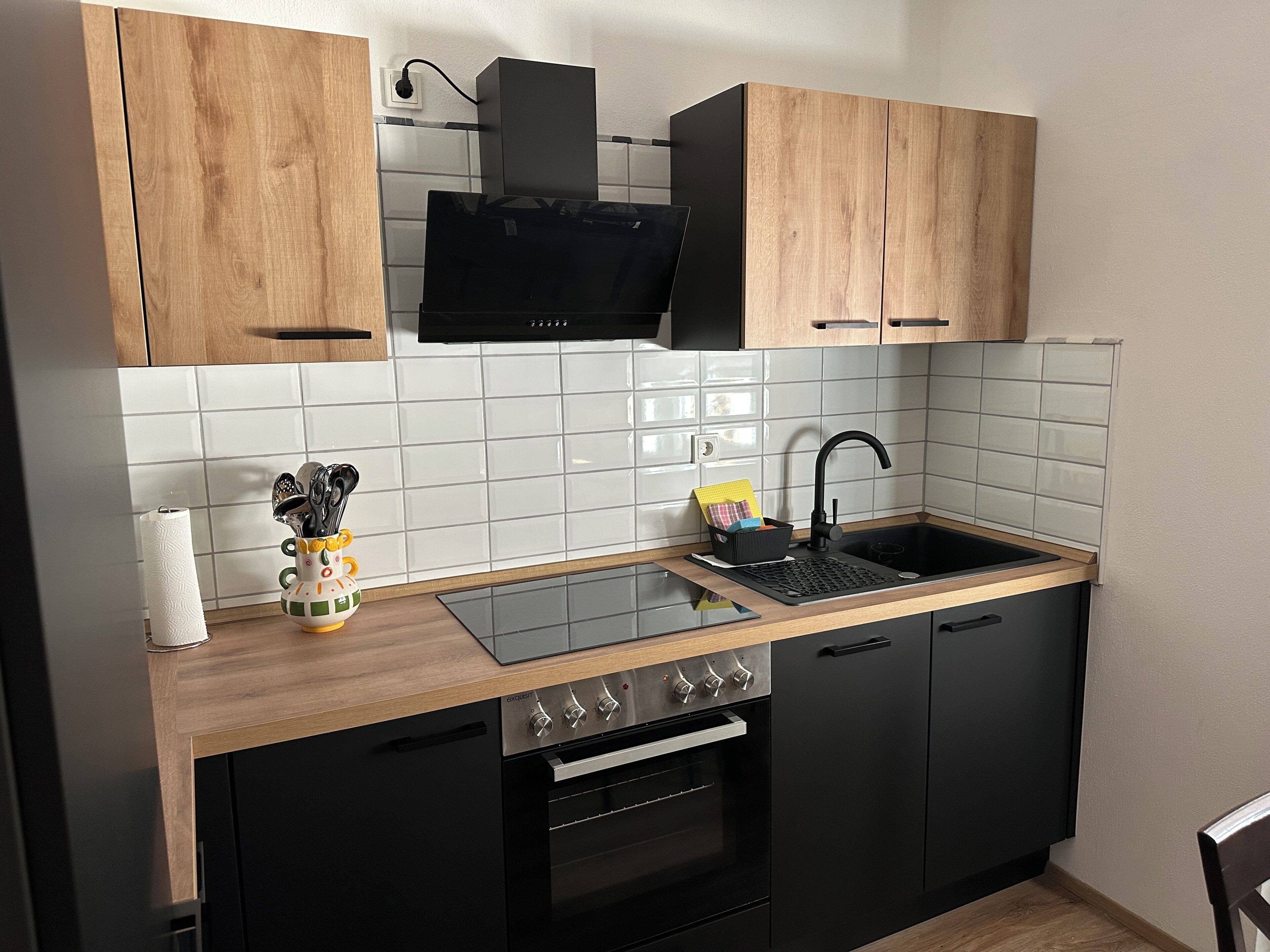 Eine kleine Küche mit einem schwarzen Ofen, einer Edelstahl-Spüle und Holzschränken.