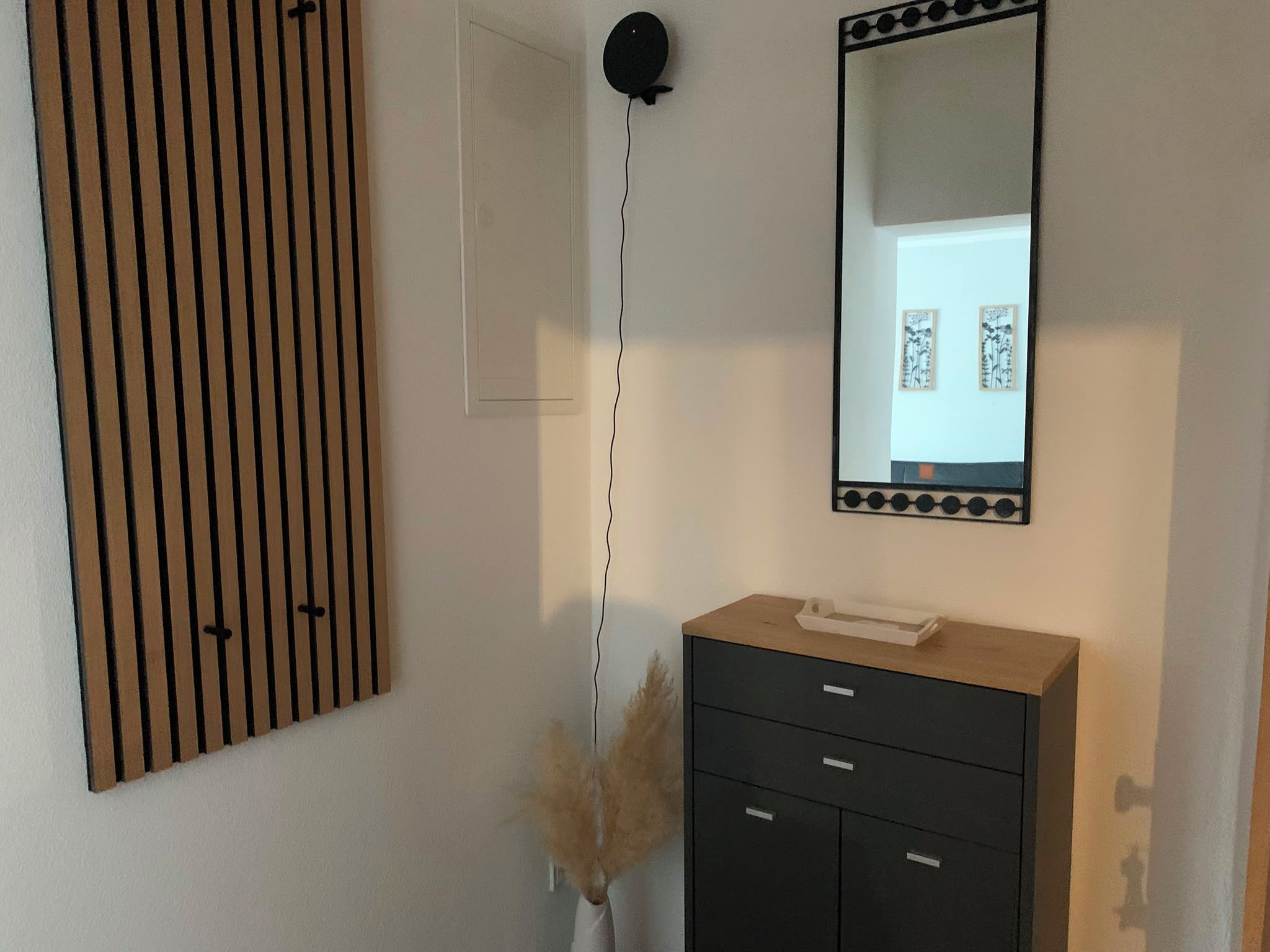 Una habitación con pared de listones de madera, tocador negro con cajones, espejo y lámpara de pared.