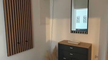 Una habitación con pared de listones de madera, tocador negro con cajones, espejo y lámpara de pared.