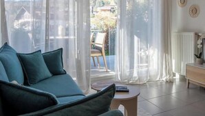 Ein Wohnzimmer mit einer Couch, einem Couchtisch und Blick ins Freie durch eine Glastür.