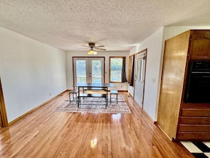 Un espace repas avec une table et des bancs en bois, un ventilateur de plafond et un coin cuisine doté de meubles en bois.