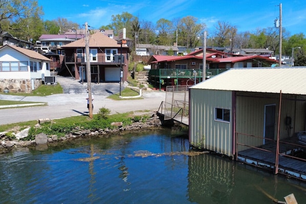 Un petit bâtiment doté d’un toit en métal, une jetée s’avançant dans une étendue d’eau et une route menant à un quartier résidentiel avec des maisons.