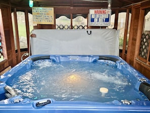 Un bain à remous entouré d’une structure en bois, agrémenté de panneaux d’avertissement et offrant une vue sur l’extérieur.