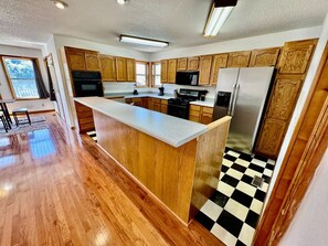 A kitchen with wooden cabinets, a central island, a black and white checkered floor, and a large window.