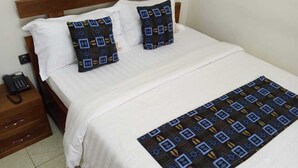 Een opgemaakt bed met witte lakens, twee gestreepte kussens, een houten hoofdbord en een telefoon op het nachtkastje.