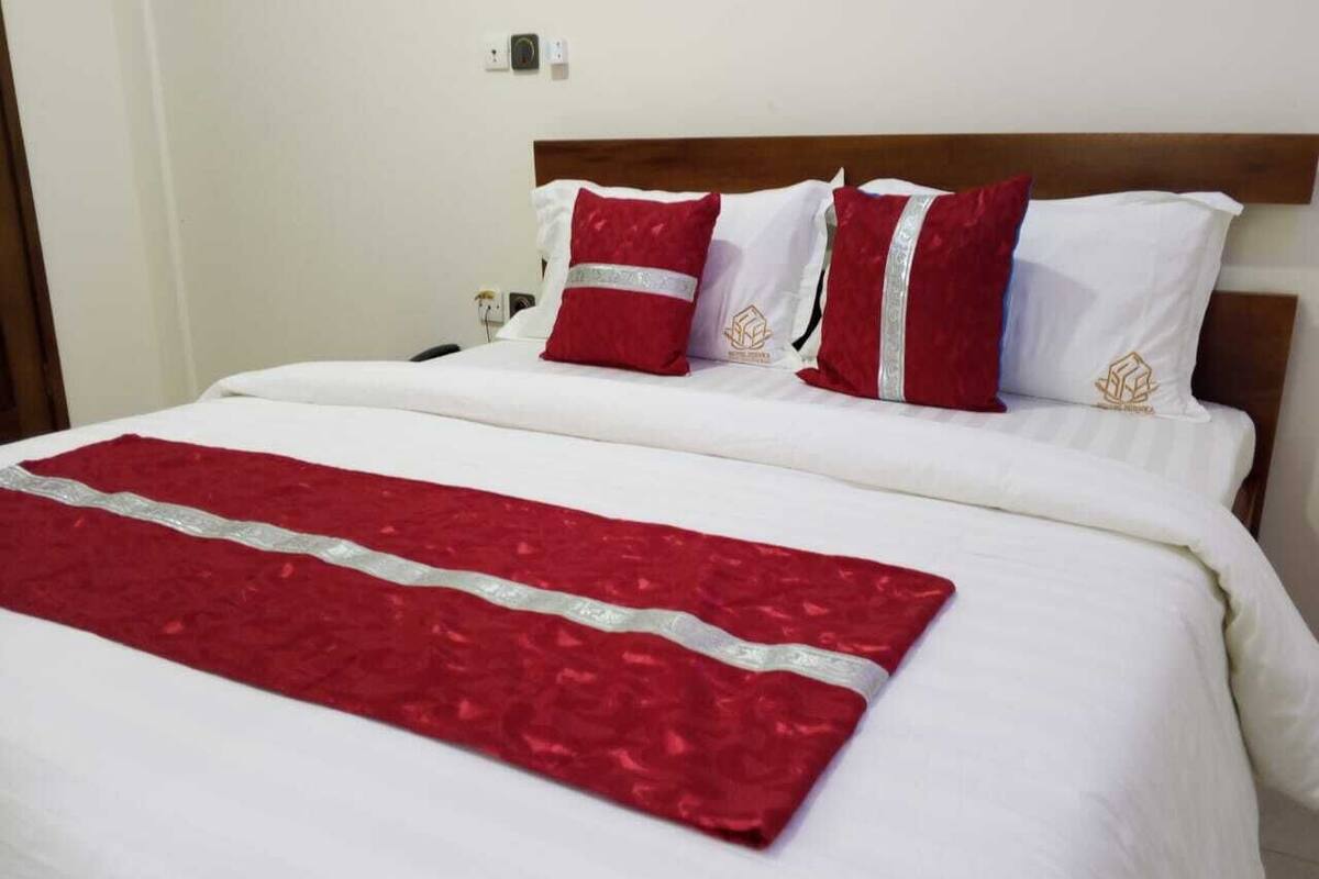 A neatly made bed with white bedding and a red decorative runner.