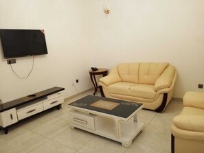 Ένα σαλόνι με έναν καναπέ, ένα τραπεζάκι σαλονιού, μια τηλεόραση και ένα βοηθητικό τραπεζάκι.