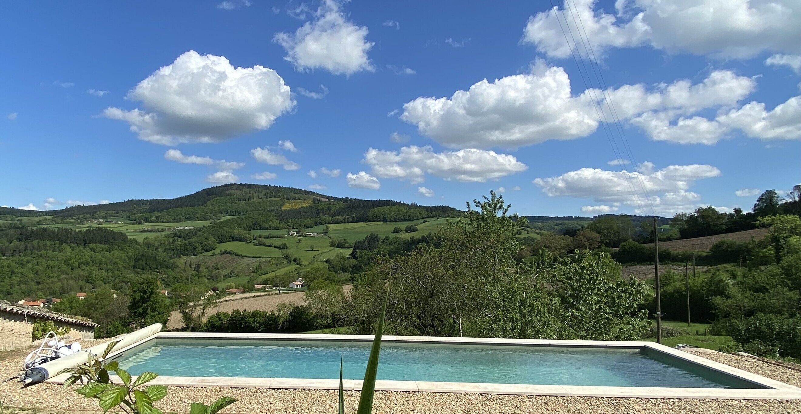 Une piscine rectangulaire, avec un ciel bleu clair et quelques nuages épars en arrière-plan.