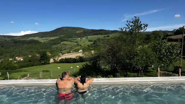 En pool med klart vand, omkranset af et hegn, med udsigt til grønne bakker og et bjerg i baggrunden.