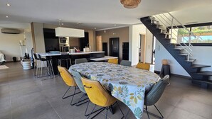 Eine moderne Küche mit einer zentralen Kochinsel, einem Essbereich mit Tisch und Stühlen sowie einer Treppe, die in einen oberen Bereich führt.