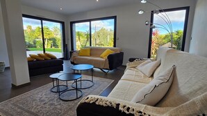 Ein modernes Wohnzimmer mit einer Couch, Sesseln, einem Couchtisch und Blick durch große Fenster.