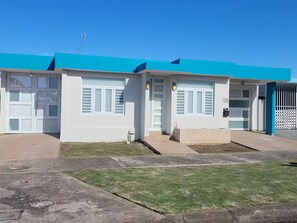 Un edificio con techo azul, paredes exteriores blancas y entrada protegida por una reja.