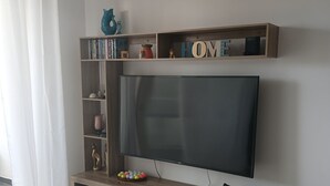 Ein modernes Wohnzimmer mit Flachbildfernseher, Holzregalen und einem weißen Vorhang.