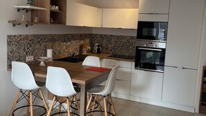 Eine moderne Küche mit weißen Schränken, einem Holztisch mit vier Stühlen, einer Pendelleuchte und einer Mikrowelle.