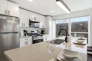 A modern kitchen with white cabinets, stainless steel appliances, a large window, and a dining area with a glass table. - Central & Comfortable Two Bedroom Two Bathroom (Cleveland)
