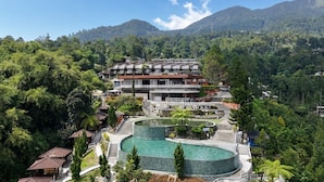 Un resort con piscina, un edificio de varios pisos y montañas al fondo.