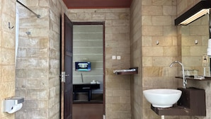 Un baño con pared de piedra, puerta de madera, lavabo, espejo y una pantalla digital que muestra información.