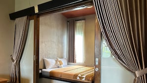 Una habitación pequeña con cama, cortinas, un banco de madera y una ventana.