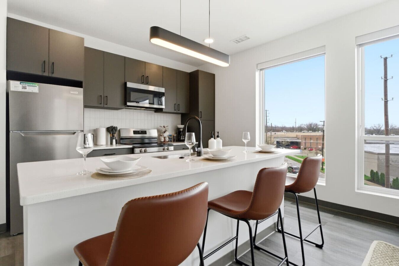 A modern kitchen with a central island, bar stools, and a view of a parking lot.