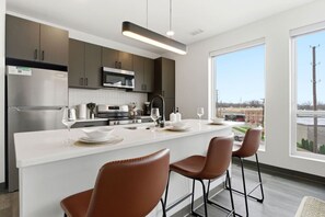 A modern kitchen with a central island, bar stools, and a view of a parking lot. - Relaxing & Central Two Bedroom Two Bathroom (Cleveland)