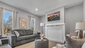 A living room with a grey sofa, a round coffee table, a fireplace, and a cityscape painting on the wall. - Cozy & Spacious Four Bedroom (Cleveland)