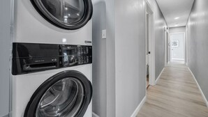 A laundry room with two front-loading washing machines, a dryer, and a control panel. - Cozy & Spacious Four Bedroom (Cleveland)