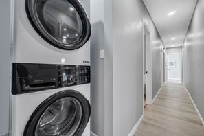 A laundry room with two front-loading washing machines, a dryer, and a control panel. - Cozy & Spacious Four Bedroom (Cleveland)