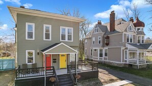 A two-story house with a front porch, a red door, and a small garden area. - Cozy & Spacious Four Bedroom (Cleveland)