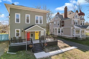 A two-story house with a front porch, a red door, and a small garden area. - Cozy & Spacious Four Bedroom (Cleveland)