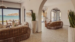 Ένας μοντέρνος εσωτερικός χώρος με έπιπλα από μπαμπού, μεγάλα παράθυρα και θέα στη θάλασσα.