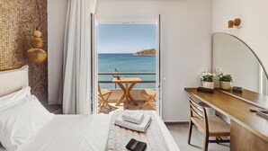 Une chambre d’hôtel avec un lit, un bureau, une chaise, une petite table et une vue sur la mer.