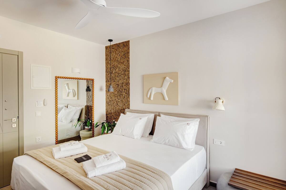 A hotel room with a bed, a mirror, a wall-mounted light, and a small plant.