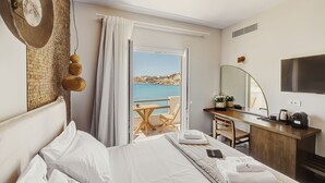 Une chambre d’hôtel avec un lit, un bureau et une chaise, une télévision et une vue sur la mer.